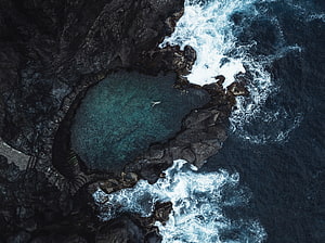 Aerial View of Turquoise Coastal Lagoon Surrounded by Dark Volcanic Rocks and White Ocean Waves HD wallpaper