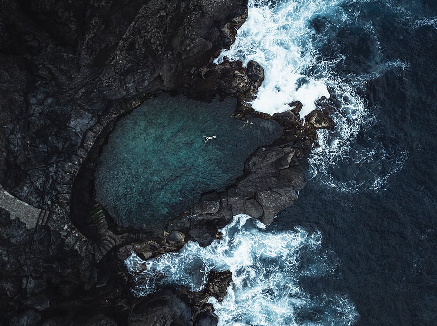 Aerial View of Turquoise Coastal Lagoon Surrounded by Dark Volcanic Rocks and White Ocean Waves HD wallpaper