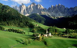 Alpine Village with Church Nestled in Green Meadows Beneath Dramatic Dolomite Peaks HD wallpaper