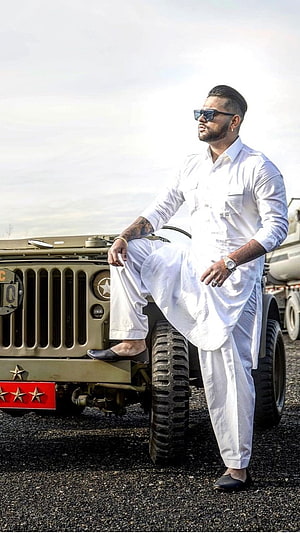 Karan Aujla in white kurta and sunglasses posing beside a military jeep HD phone wallpaper