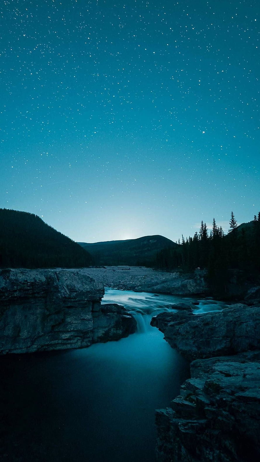 Starry Night Sky Over a Rocky River Canyon with Distant Mountains and Pine Trees HD phone wallpaper