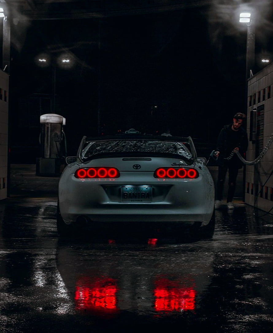 Rear View of a Silver Toyota Supra at a Nighttime Gas Station with Wet Pavement Reflections HD phone wallpaper
