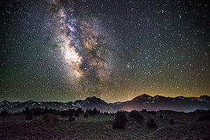 Milky Way Galaxy Arching Over Snow-Capped Mountain Ranges Under a Star-Filled Night Sky HD wallpaper