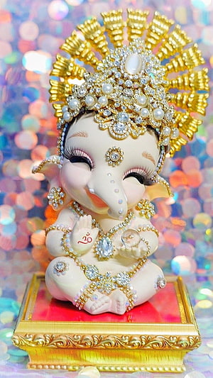 Adorned Baby Ganesha Idol With Golden Crown And Jewels On Ornate Red Base HD phone wallpaper