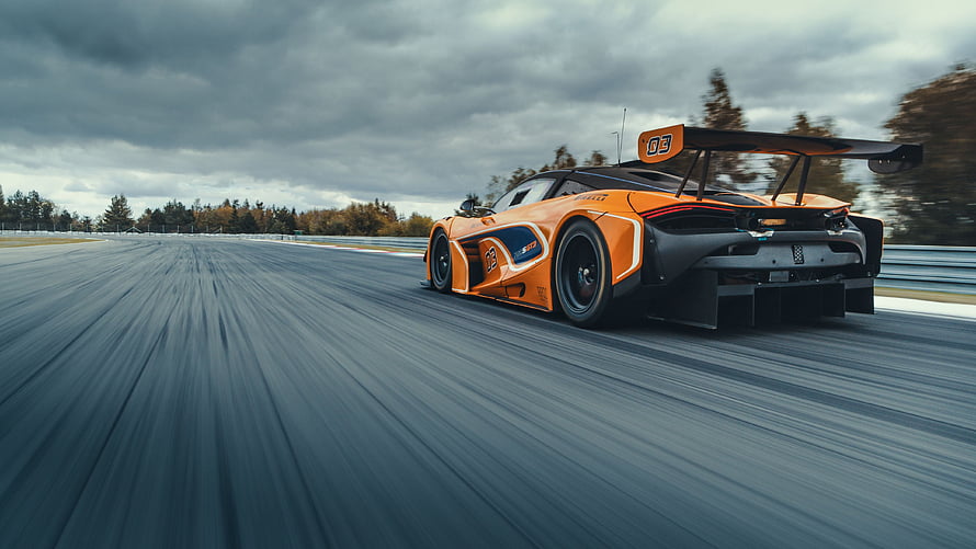 McLaren 720S GT3 race car speeding on a track under a dramatic overcast sky HD wallpaper