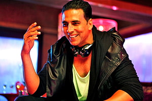 Akshay Kumar in a black leather jacket with headphones around his neck in a vibrant club setting HD wallpaper