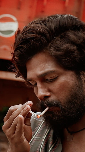Allu Arjun as Pushpa lighting a cigarette in a moody close-up portrait HD phone wallpaper