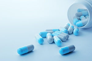 Blue and white pharmaceutical capsules spilling from a bottle on a clean clinical surface HD wallpaper