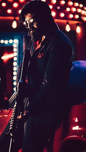 Rocky Bhai from KGF in a moody neon-lit scene with sunglasses and a rifle HD phone wallpaper