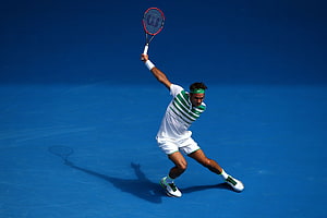 Roger Federer serving on a blue hard court in a white and green striped outfit HD wallpaper