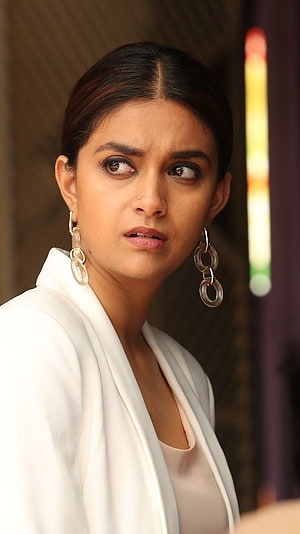 Keerthi Suresh in a white blazer with statement hoop earrings and a serious expression HD phone wallpaper