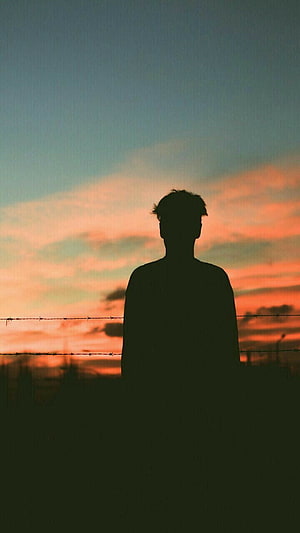 Silhouette of a Young Man Standing Before a Vibrant Orange and Blue Sunset Sky HD phone wallpaper