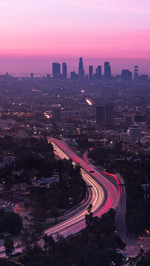 Los Angeles skyline at dusk with long exposure highway light trails and pink sunset sky HD phone wallpaper