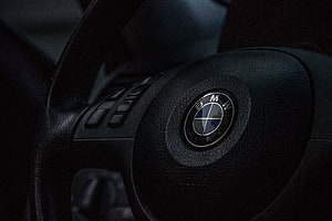 Close-up of a BMW steering wheel center hub with the iconic roundel logo on textured black leather HD wallpaper