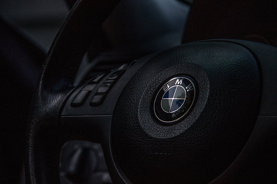 Close-up of a BMW steering wheel center hub with the iconic roundel logo on textured black leather HD wallpaper
