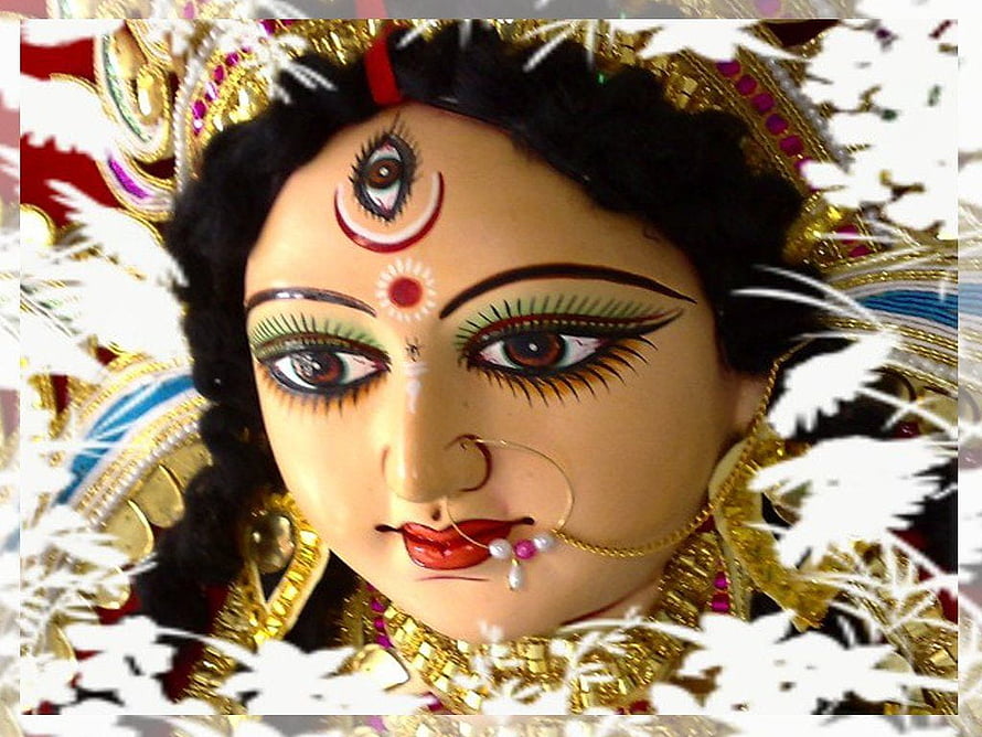 Close-up of Durga Maa idol with third eye, ornate gold jewelry, and white floral border HD wallpaper