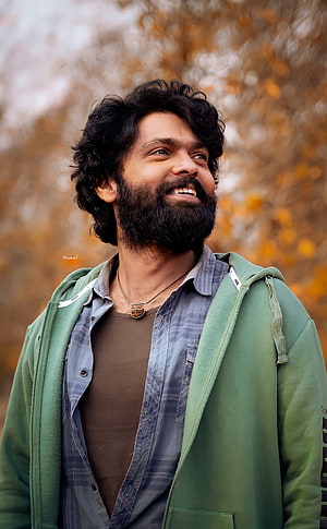 Rakshit Shetty smiling portrait in green jacket with autumn foliage background HD phone wallpaper