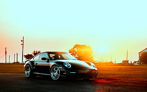 Black Porsche 911 Turbo S parked on a rural road at golden hour with warm sunset glow HD wallpaper