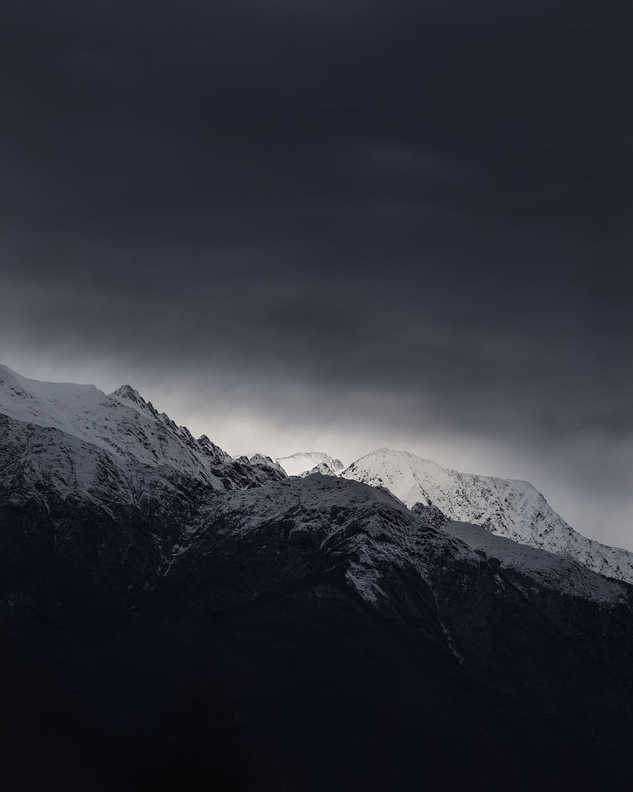 Moody Snow-Capped Mountain Peaks Under a Heavy Stormy Sky HD phone wallpaper