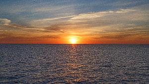 Golden sunset over a calm ocean horizon with scattered clouds and warm sky reflections HD wallpaper