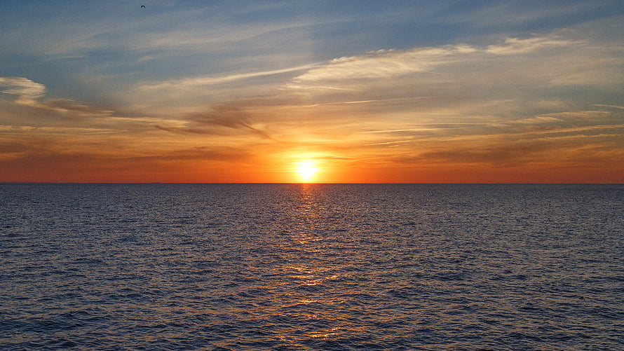 Golden sunset over a calm ocean horizon with scattered clouds and warm sky reflections HD wallpaper