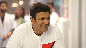 Puneeth Rajkumar smiling in a white t-shirt with a red graphic design HD wallpaper