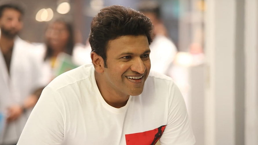 Puneeth Rajkumar smiling in a white t-shirt with a red graphic design HD wallpaper