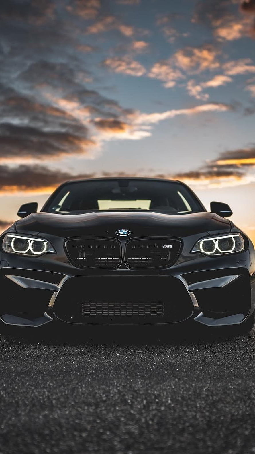 Black BMW M2 Front View at Sunset with Dramatic Clouds and Aggressive Grille Design HD phone wallpaper