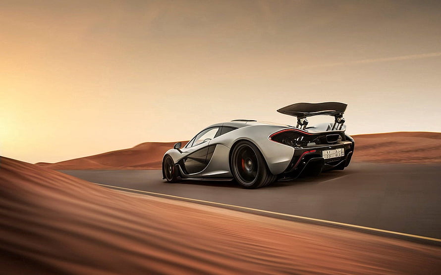 McLaren P1 supercar speeding along a desert road at golden hour with dramatic rear wing HD wallpaper