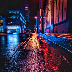 Neon-lit wet city street at night with vivid red and blue reflections on rain-soaked asphalt HD phone wallpaper