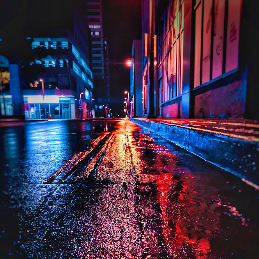 Neon-lit wet city street at night with vivid red and blue reflections on rain-soaked asphalt HD phone wallpaper