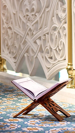 Open Quran on a wooden stand inside a mosque with ornate white lattice screen and patterned carpet HD phone wallpaper