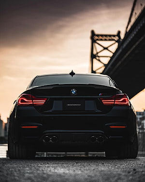 Rear View of a Black BMW M4 Competition Sedan Parked Under a Steel Bridge at Sunset HD phone wallpaper