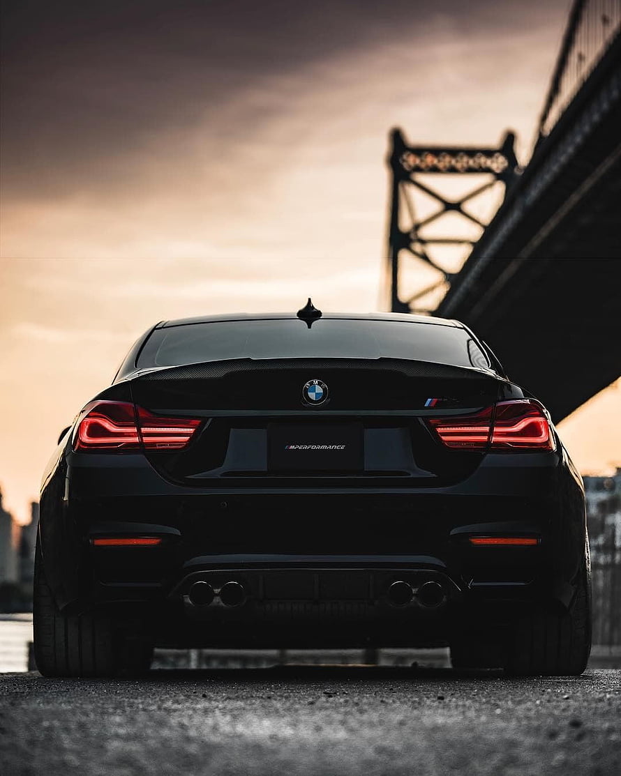 Rear View of a Black BMW M4 Competition Sedan Parked Under a Steel Bridge at Sunset HD phone wallpaper