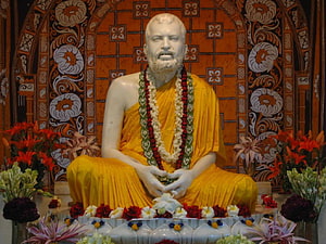 Sri Ramakrishna Statue in Yellow Robes with Floral Garlands and Ornate Backdrop HD wallpaper