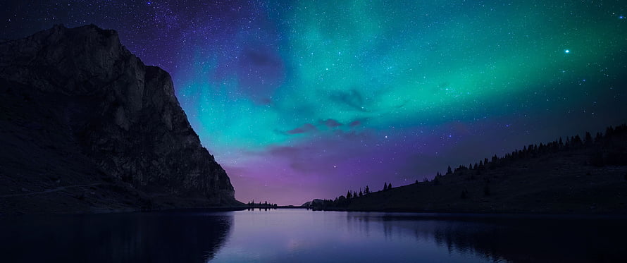 Vivid Green and Purple Aurora Borealis Dancing Over a Serene Mountain Lake at Night HD wallpaper