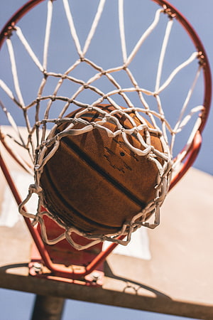 Close-up of a basketball resting in a white net against a clear blue sky HD phone wallpaper