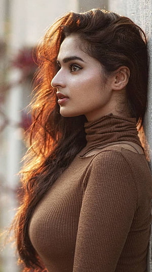 Ayesha Khan in a brown turtleneck with long wavy hair in warm golden light HD phone wallpaper