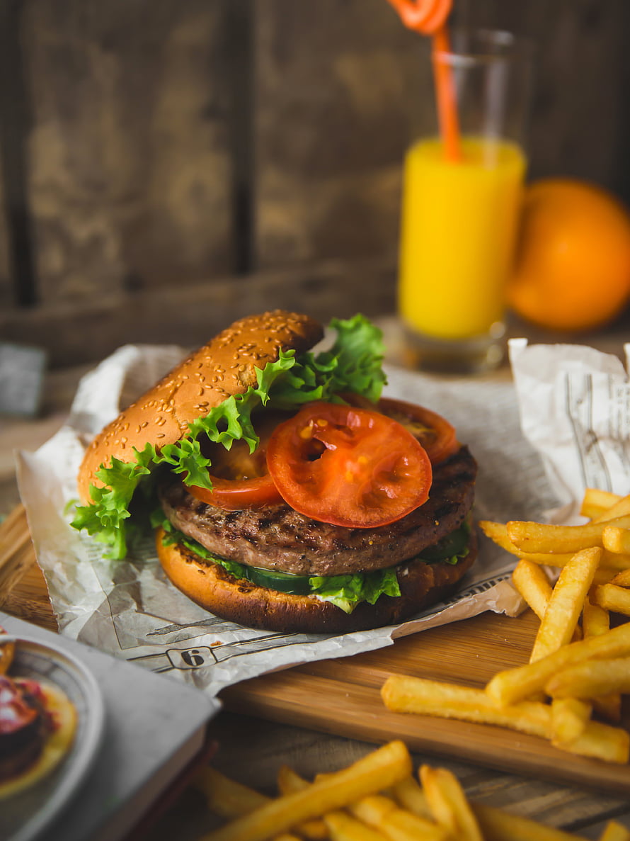 Gourmet beef burger with fresh lettuce, tomato, and golden fries on a rustic wooden board HD phone wallpaper