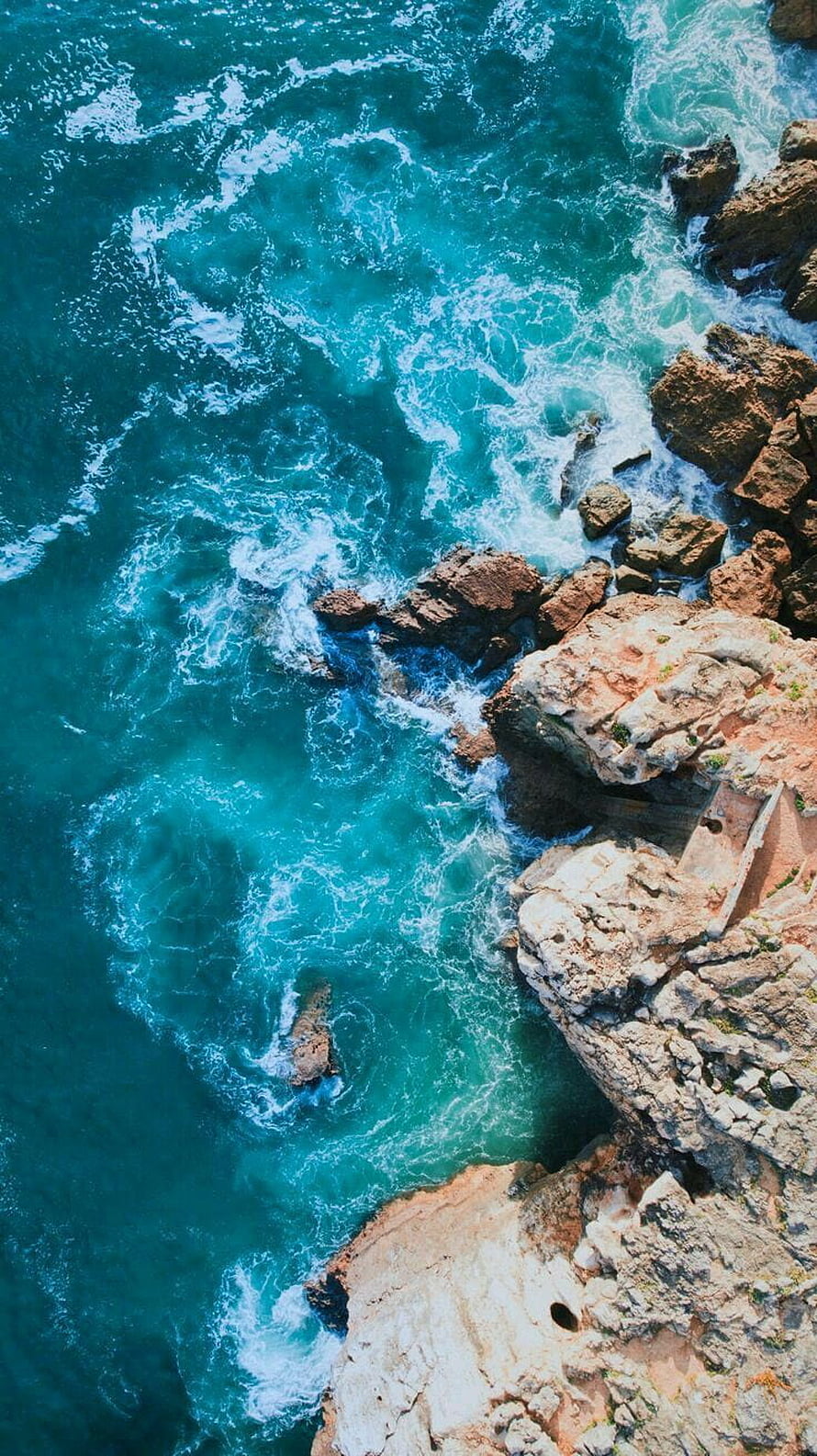 Aerial View of Turquoise Ocean Waves Crashing Against Rugged Coastal Cliffs HD phone wallpaper