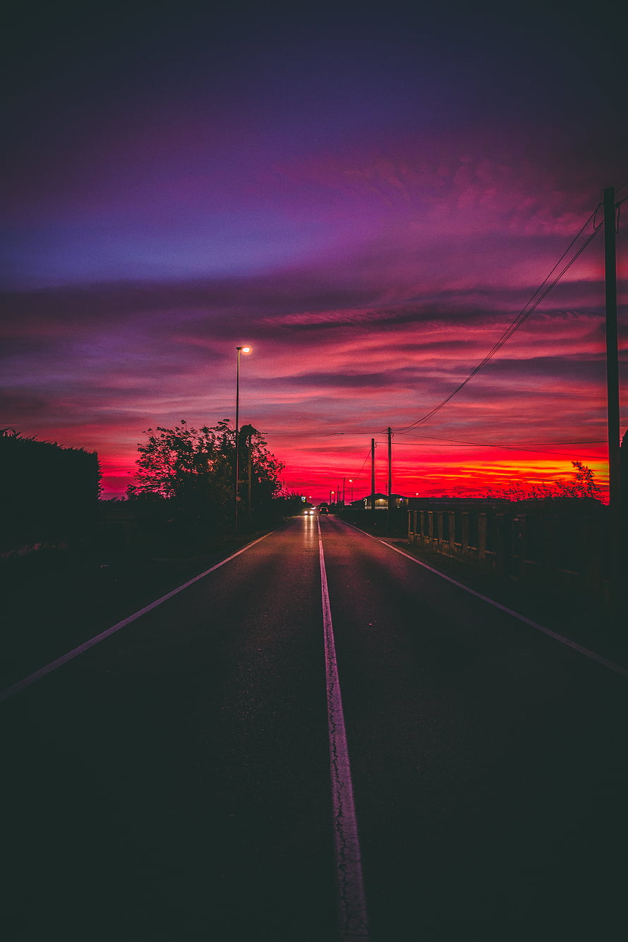 Vivid Crimson and Purple Sunset Over a Dark Two-Lane Highway at Dusk HD phone wallpaper