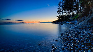 Serene Twilight Shoreline with Smooth Water and Pebble Beach HD wallpaper