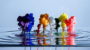 Vibrant multicolored ink clouds blooming in water with ripples and reflections HD wallpaper