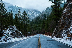 Winding Mountain Road Through Snowy Pine Forest Under Overcast Winter Sky HD wallpaper
