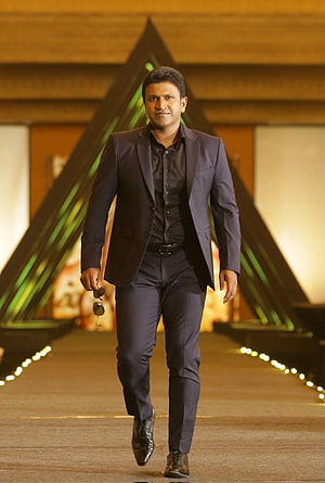 Punit Rajkumar in a dark suit walking on a runway at a film event HD phone wallpaper