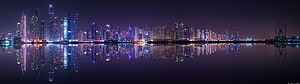 Panoramic Night Skyline with Vibrant Purple and Blue City Lights Reflected in Calm Water HD wallpaper