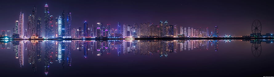 Panoramic Night Skyline with Vibrant Purple and Blue City Lights Reflected in Calm Water HD wallpaper