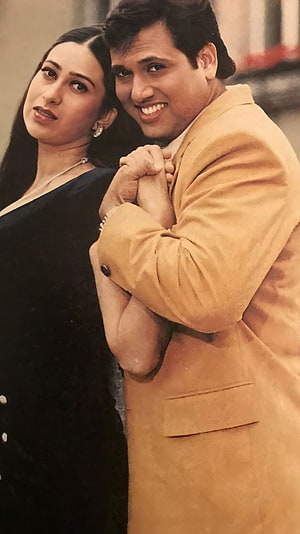 Govinda and Karishma Kapoor in a warm embrace from a classic Bollywood film HD phone wallpaper