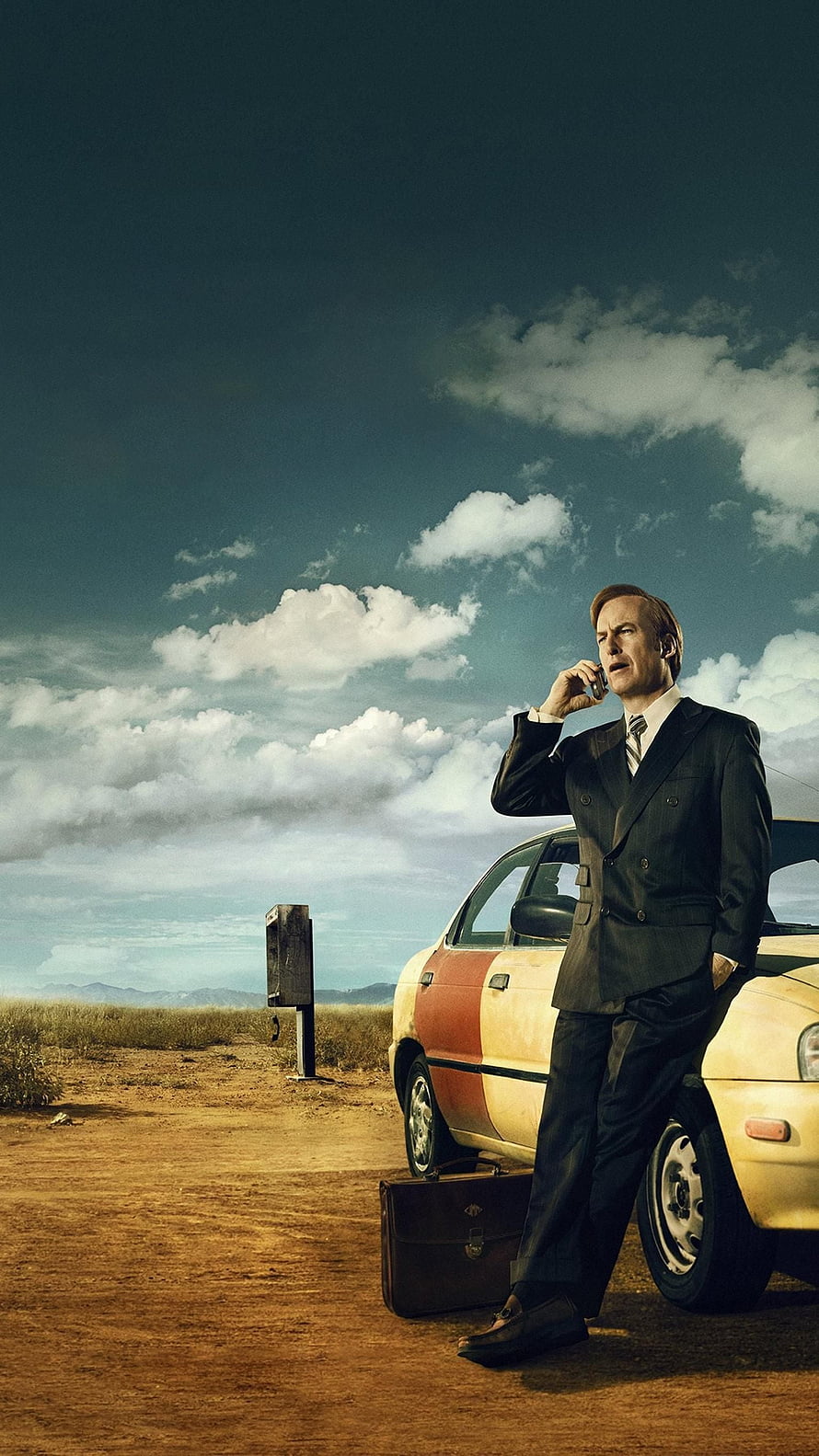 Saul Goodman in a dark suit leaning against a car in a desert landscape while talking on a phone HD phone wallpaper