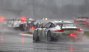 Porsche 911 RSR race car navigating wet track in heavy rain with spray and other competitors HD wallpaper